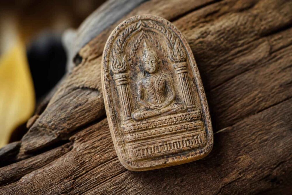 Rzeźbiony drewniany amulet przedstawiający siedzącego Buddy na tle desek
